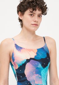 Maillot de bain une pièce avec un motif floral dans des teintes de bleu et de corail. Fabriqué en tissu extensible avec de fines bretelles.