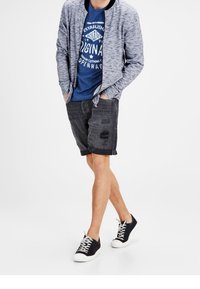 Grå stickad bomberjacka över blå grafisk t-shirt, kombinerad med svarta denimshorts med ett hål och svarta snörskor.