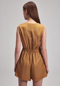 Mono sin mangas de color mostaza con cintura elástica, textura suave y corte relajado, que presenta pantalones cortos con dobladillos enrollados.