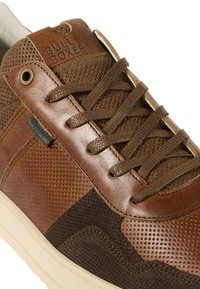 Sneaker in pelle marrone con una combinazione di texture lisce e perforate, sfumature di marrone a contrasto e sei occhielli per i lacci. Nome del marchio impresso sulla linguetta.