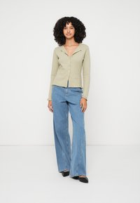 Svetlo zelena rebrasta bluza z gumbi in ovratnikom, kombinirana z ohlapnimi, visoko pasnimi modrimi jeans hlačami in črnimi čevlji s koničastim prstom.