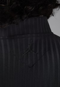 Fekete csíkozott anyagú, magas nyakú, a hátoldalán finom fekete hímzett Jumpman logóval, amely modern és elegáns megjelenést kölcsönöz.