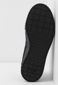 Semelle de chaussure noire avec des motifs de grille et de bande de roulement, affichant un logo Puma près du talon sur un fond blanc.