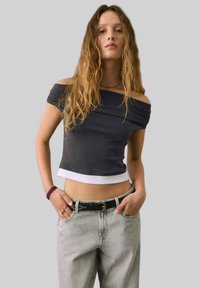 Top scurt negru, cu umeri descoperiți, având o margine albă, asortat cu blugi gri deschis, cu talie înaltă și un brâu negru cu ținte.