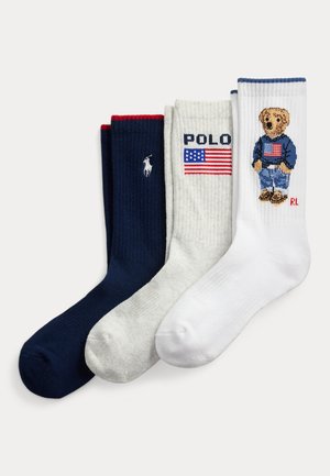 Kolme taiteltua sukkaa marineen sinisenä, valkoisena ja kermansävyisenä; marineen sinisessä valkoinen polo-pelaajan logo, kermansävyisessä "POLO" ja Yhdysvaltain lippu, valkoisessa karhu, jolla on amerikkalaislippuinen villapaita.