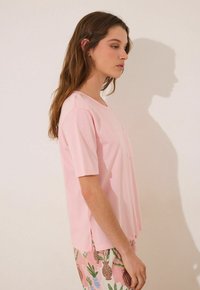 T-shirt rosa a maniche corte con collo rotondo e dettaglio della tasca, realizzato in tessuto morbido, abbinato a pantaloni a fantasia rosa chiaro.