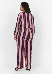 Combinaison longue présentant des rayures verticales en rose, marine, bordeaux et or. Fabriquée en tissu léger avec une coupe décontractée et une taille élastique.