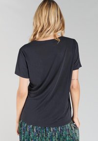 T-shirt noir à manches courtes avec une coupe décontractée, texture lisse, encolure ronde et un design de dos drapé. Détails de couture subtils visibles.