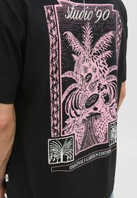 Sort t-shirt med et stort pink botanisk grafisk design, dekoreret med kanter og teksten "Studio '90", mærket "Originals Garden Edition."
