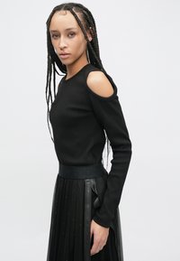 Melnas garām piedurknēm virskrekls ar izgriezumiem uz pleciem, kopā ar caurspīdīgu melnu svārku, kas ir ar teksturētu jostasvietu un dekoratīvām lentēm.