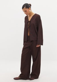 Rjav, ohlapen zgornji del z V-izrezom in vezavami spredaj, v kombinaciji s širokimi hlačami v enaki barvi. Gladka tekstura. Minimalističen dizajn.