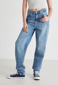 Jeans de tiro alto, de color azul claro y corte holgado, con cinco bolsillos, pasadores para cinturón y cierre de botón, combinados con zapatillas de deporte de color azul oscuro.