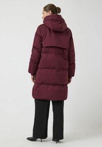 Vinrød dunjakke med hette, med quiltet design, stor bakpanel og elastiske mansjetter, kombinert med svarte bukser.