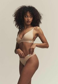 Nude triangel-bra och matchande trosor, gjorda av ett mjukt material, med minimalistisch design och subtila märkesdetaljer.