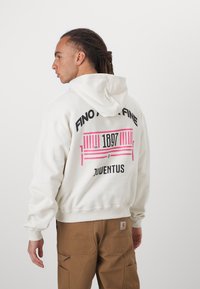 Fehér kapucnis pulóver, hátul nagyméretű grafikai dizájnnal rózsaszín és fekete színekben, feliratok: "FINO ALLA FINE," "1897," és "JUVENTUS."