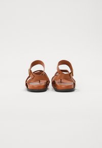 Sandales en cuir marron avec un design à sangles croisées, semelles plates et une fermeture à boucle pour un ajustement réglable. Fini texturé et lisse.