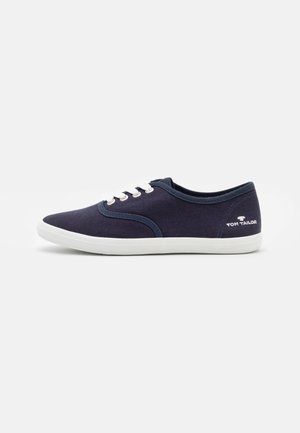 Zapatillas de lona azul marino con suelas y cordones de caucho blanco. Presentan punta redondeada y el logo "TOM TAILOR" en el talón. Textura suave.