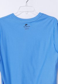 Svetlo modra Nike majica s kratkimi rokavi in okroglim ovratnikom, na hrbtni strani ima majhen črn logotip in napis. Mehka tkanina z gladko teksturo.