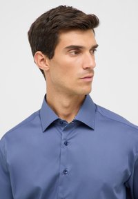 Camicetta azzurro chiaro con una texture liscia, colletto a punta e fodera interna del colletto a motivo contrastante, dotata di bottoni discreti.