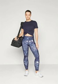 Tumesinine lühike t-särk sõlmega ees, koos kõrge vöökohaga retuusidega, millel on sinise ja valge marmoriga muster. Must spordikott ja valged tossud.