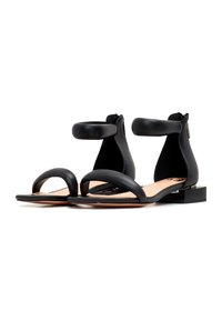 Sandales noires à bout ouvert avec brides rembourrées à la cheville, petits talons bloc et semelle beige sur fond blanc.
