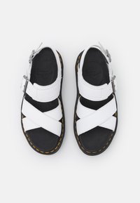 Sandales en cuir blanc avec semelles noires, surpiqûres jaunes, deux brides croisées et boucles ajustables à la cheville, vues de dessus.