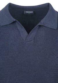 Navyblauwe polo-shirt met een gestructureerd breisel, een V-hals en een platte kraag. Etiket geeft "SUITABLE" aan.