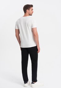 Lys grå spraglet t-shirt og sorte bukser. T-shirten har korte ærmer og standard rund halsudskæring; bukserne har slim-fit med sidelommer. Hvide sneakers fuldender looket.