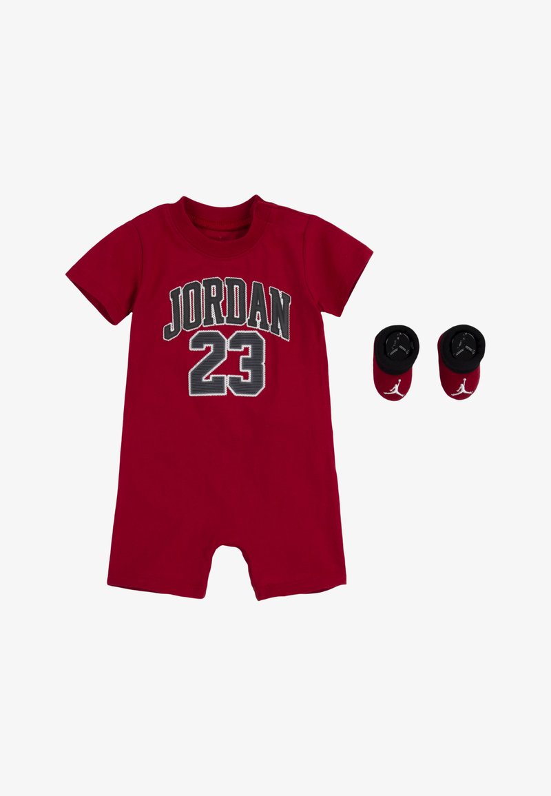 Raudonas medvilninis trumpas rankovėmis kūdikių bodysuitas su užrašais "JORDAN" ir "23" juodai baltomis raidėmis. Komplekte yra atitinkamos juodos ir raudonos kojinaitės.
