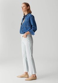 Denim blouse, blauw, lange mouwen. Lichtblauwe, rechte spijkerbroek. Beige, puntige ballerina's. Eenvoudig ontwerp met minimale details.