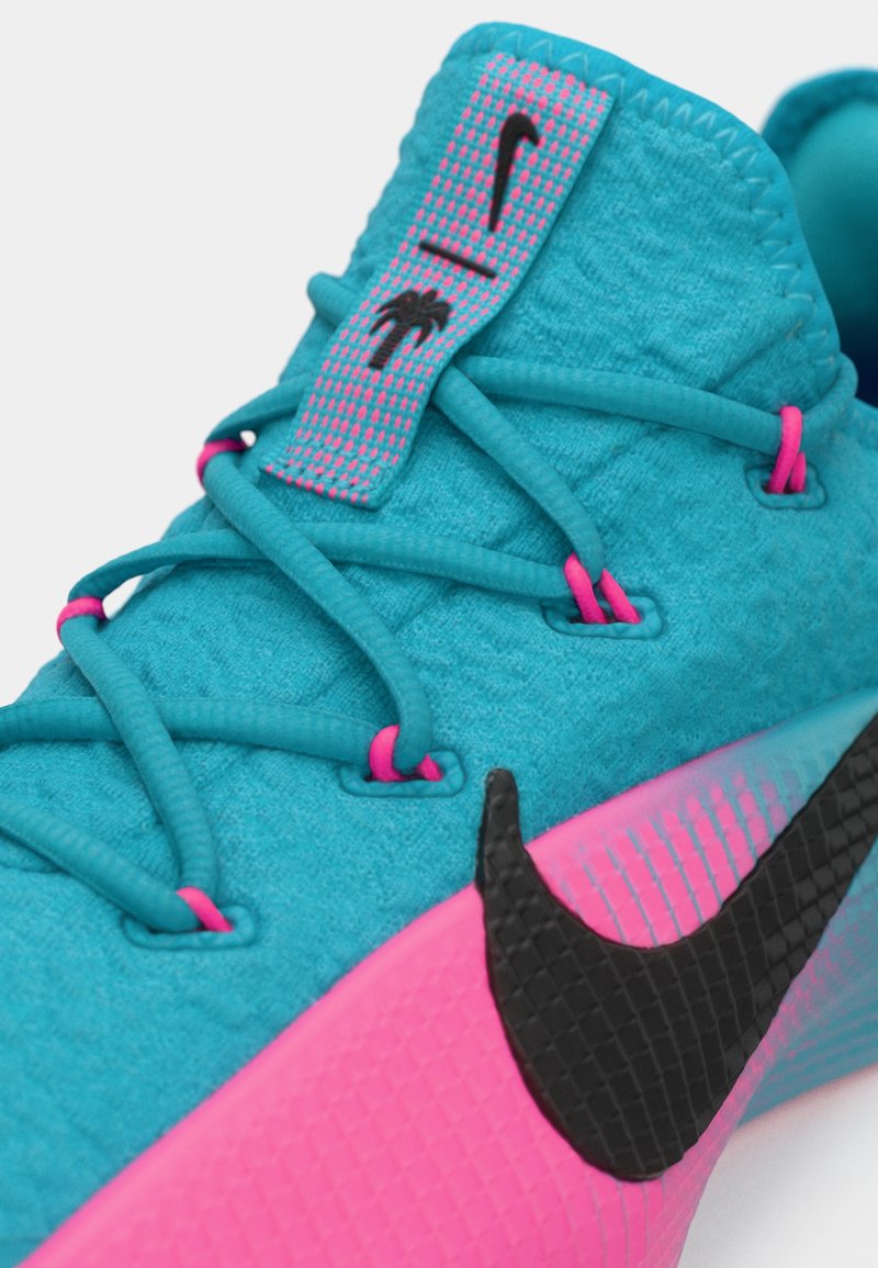 Zapatilla deportiva azul y rosa con el logo negro de Nike, cordones azules y ganchos de cordones rosas sobre un fondo blanco.