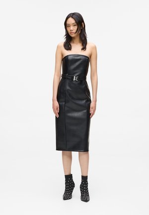 Abito senza spalline in pelle nera con un design aderente, lunghezza knee-length e vita con cintura. Paio di stivali neri alla caviglia con borchie argentate.