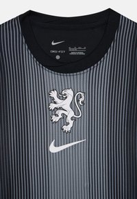 Nike Dri-FIT t-shirt i grått och svart med vertikala ränder, har en vit lejonlogotyp och Nike-swoosh. Rund halsringning och mjuk textur.
