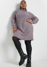 Langärmliges Kleid mit Reißverschlusskragen aus weichem lavendelfarbenem Stoff, das einen lässigen Schnitt und einen abgerundeten Saum aufweist. Kombiniert mit schwarzen Leggings und klobigen Stiefeln.