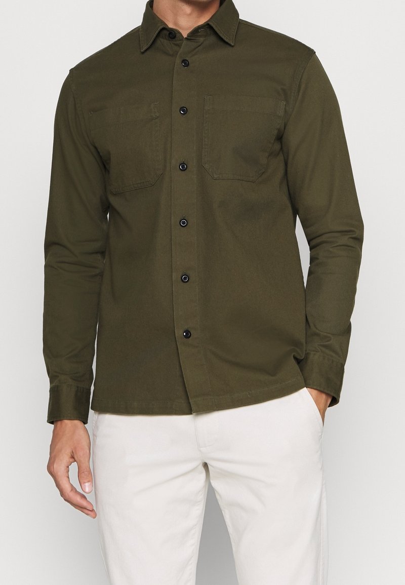Dunkelolivgrünes Hemd zum Knöpfen mit zwei Brusttaschen, schwarzen Knöpfen und klassischem Kragen; gefertigt aus einem glatten, strukturierten Material.