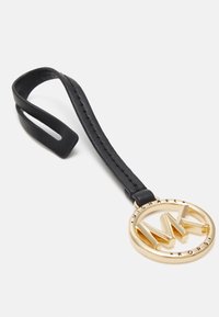 Cinturino in pelle nera con cuciture, attaccato a un logo circolare dorato con le iniziali "MK" e il nome del marchio "MICHAEL KORS" lungo il bordo.