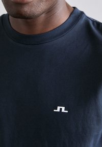 Marineblå bomulds crewneck t-shirt med et lille hvidt abstrakt logo på venstre brystområde, glat tekstur og normal pasform.