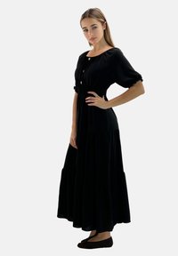 Abito maxi nero con maniche a palloncino corte, vita smock e gonna a più strati. Presenta un colletto rotondo e chiusura a bottone sul davanti.