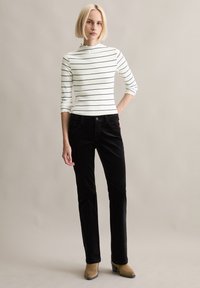 Zwart-wit gestreepte lange mouwen top, gecombineerd met zwarte corduroy broek. De top heeft een golvende halslijn, een slanke pasvorm en een zachte textuur.