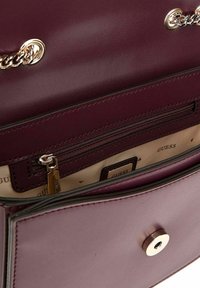 Sac à main en cuir bordeaux avec des accents en chaîne dorée, poche zippée et doublure intérieure présentant une marque imprimée. Détail de fermeture à pression visible.