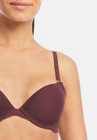 Burgundy vadderad bh med spetskant, justerbara axelband och en slät yta. Har en subtil lyster och detaljer i guldton.