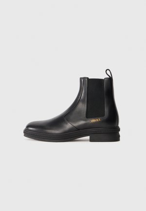 Stivaletto in pelle nera con pannello elastico laterale, tacco basso, linguetta sul retro e logo dorato Versace vicino alla suola.