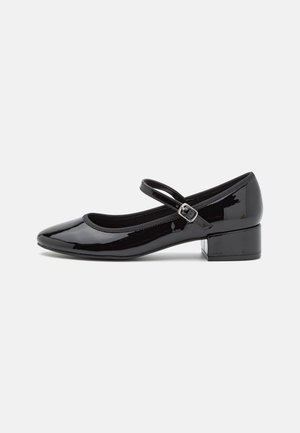 Chaussure Mary Jane en cuir verni noir avec petit talon carré et bride réglable à boucle sur fond blanc.