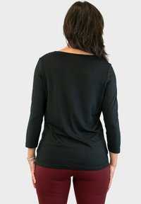 Top negro de manga larga en tejido suave con un corte relajado, cuello alto y dobladillo curvado, combinado con leggings burdeos.