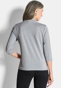 Graues Langarmoberteil mit einem subtilen Schimmereffekt, ausgestattet mit einem hohen Halsausschnitt und einem figurbetonten Schnitt, kombiniert mit schwarzen Hosen, Ansicht von hinten.