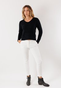 Maglione nero a v con maniche lunghe, abbinato a pantaloni bianchi aderenti e stivaletti neri alla caviglia con dettagli zip. Colori solidi, senza motivi.
