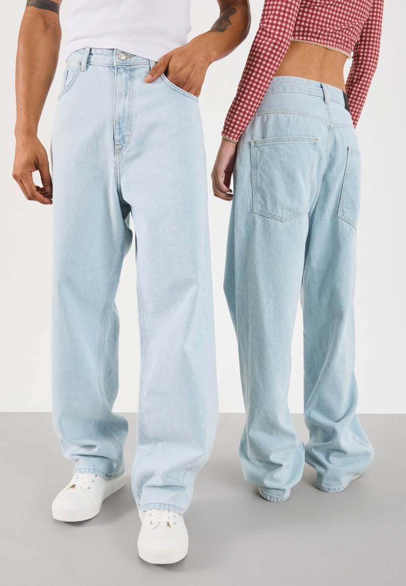 Ljusblå vida jeans med hög midja, femficksdesign och rå fåll. Matchas med vita sneakers och en röd rutig topp.