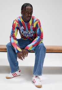 Långärmad, flerfärgad tröja med abstrakt mönster, med rund halsringning och logotyp. Kombinerad med ljusblå jeans och vita-röda sneakers.