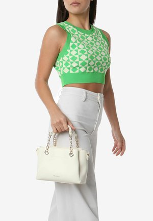 Borsa a mano bianca in pelle con manici a catena corti, caratterizzata da una texture liscia e un design minimalista, tenuta da una persona che indossa una maglietta verde a fantasia.