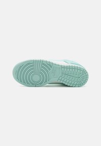 Nike sneaker with a mint green rubber sole, textured patterns, circular tread design, and branding detail. Upper features a contrasting color.